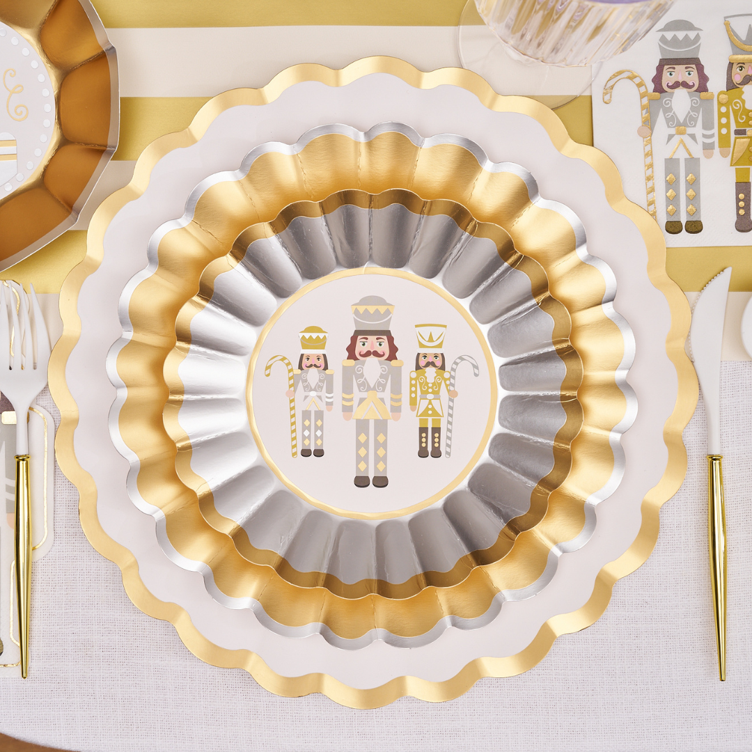 The Sophistiplate Gilded Nutcracker Table Setting features round scalloped plates with gold and silver trim and three white-and-gold nutcracker figures, perfect festive disposable tableware to pair with matching cutlery and napkins.