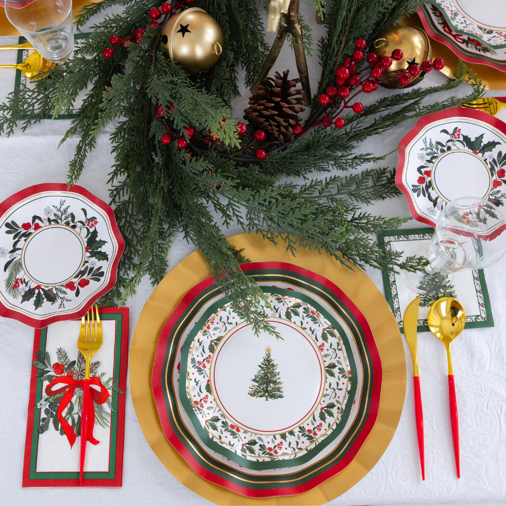 Home for the Holidays: Christmas Table for 16 featuring heavy-duty paper plates with holiday greenery, gold chargers, red and gold cutlery, and napkins with a red ribbon motif, arranged around a centerpiece of pine branches and berries.