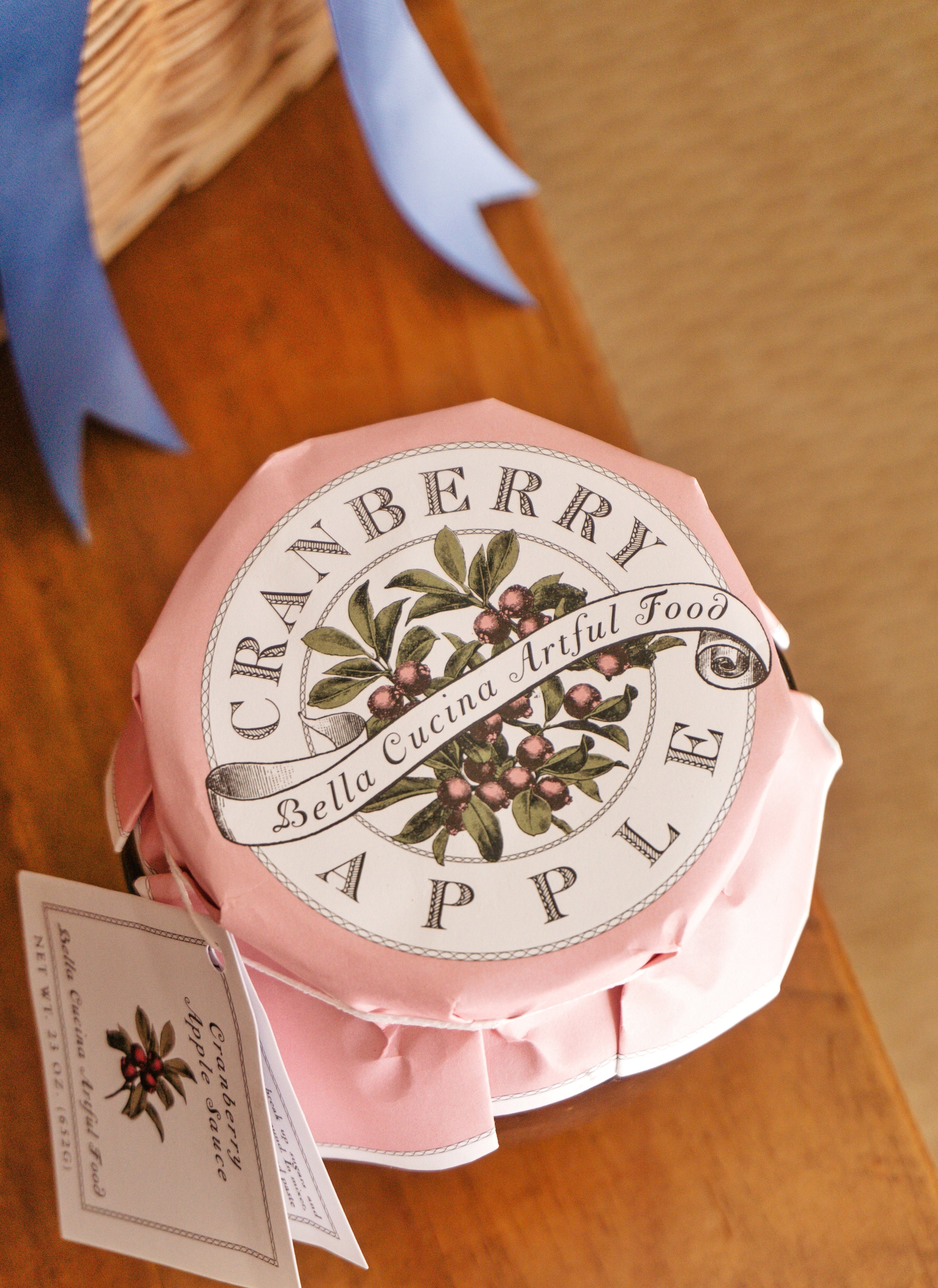 A jar of cranberry apple sauce with a pink botanical paper lid topper, placed on a Turkey & Gourds: Thanksgiving Table for 16 setting near heavy duty paper plates.