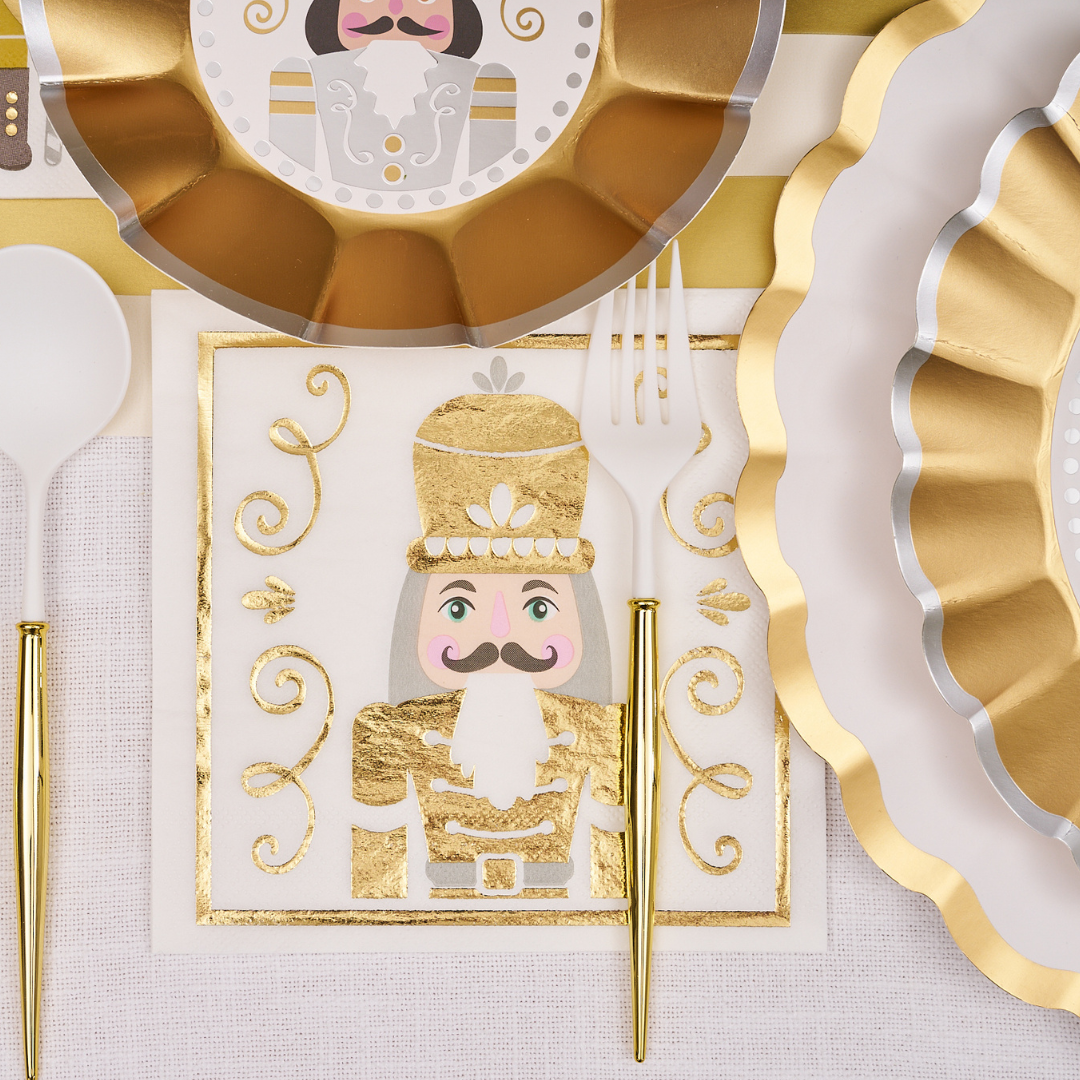 Create a festive look with the Sophistiplate Gilded Nutcracker Table Setting, featuring gold and white scalloped plates, nutcracker napkins with gold accents, and matching utensils on a crisp white tablecloth.