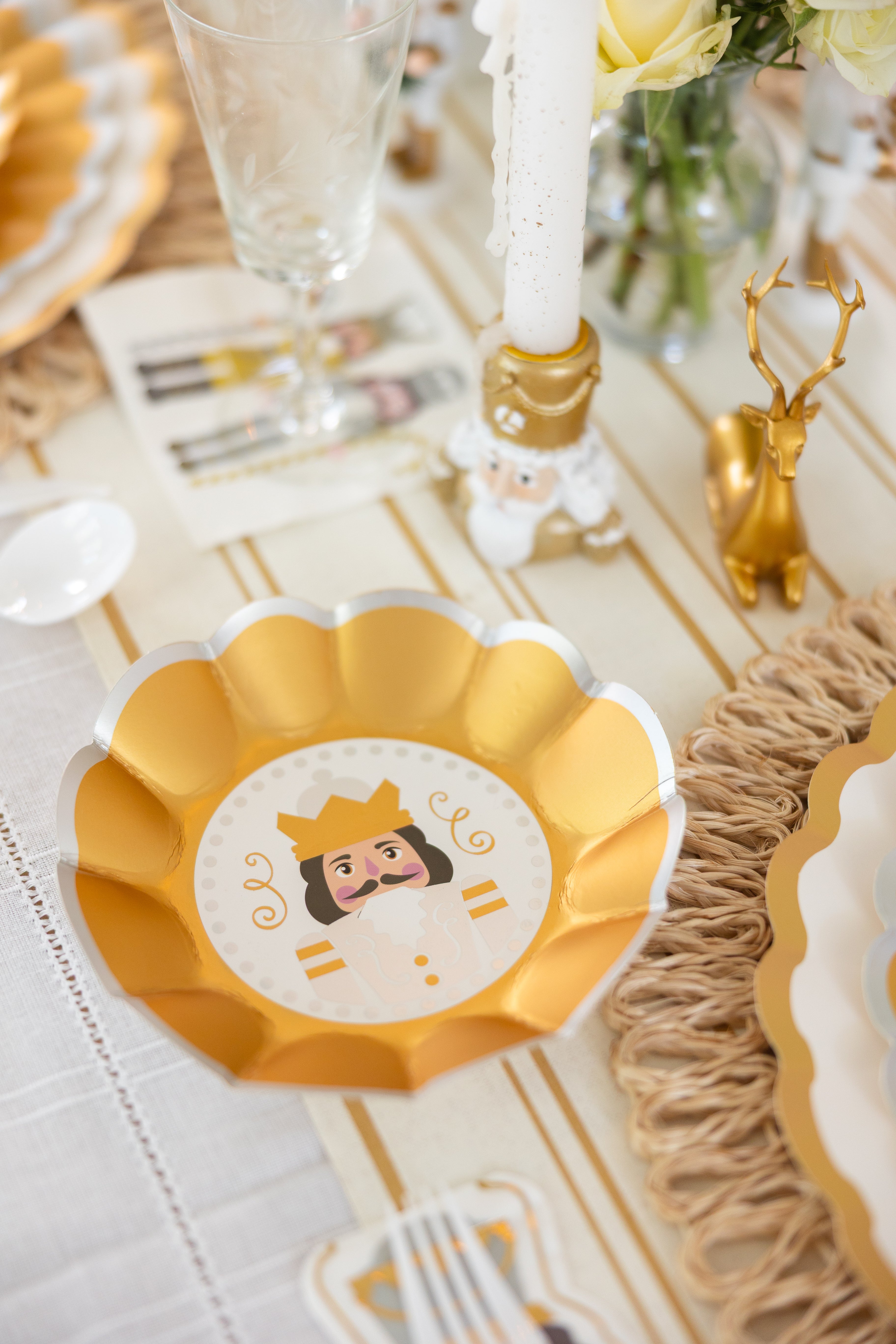 A gold and white scalloped bowl featuring a playful king design from Sophistiplate’s Gilded Nutcracker Appetizer/Dessert Bowls (8pk) adds festive flair to your holiday table, surrounded by sparkling glassware, a gold deer figurine, and a nutcracker candleholder. These charming bowls capture the spirit of special occasions with the ease and convenience of disposable tableware—making them an ideal choice for your holiday tablescape.