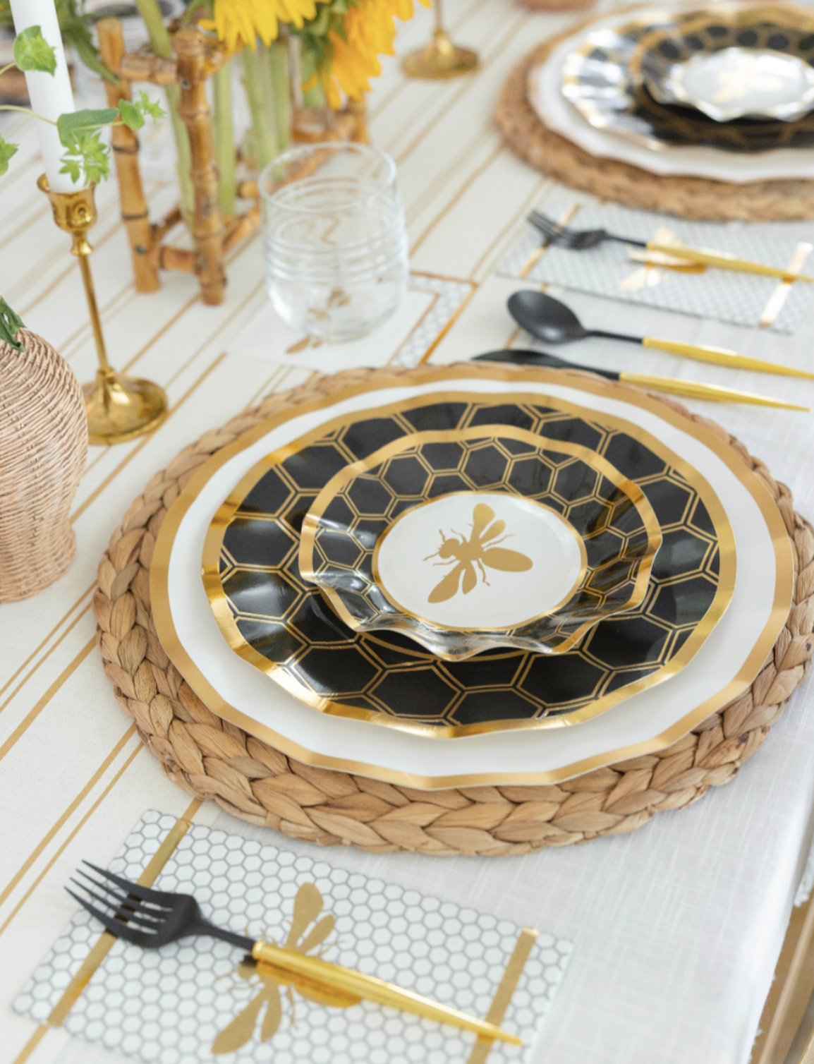 Create an elegant Rosh Hashanah tablescape with the Sophistiplate Rosh Tablescape for 16 Guests: Honeybee set. These black and gold disposable party plates feature a striking honeycomb pattern and a charming bee motif at the center, offering both beauty and durability for your celebration. Paired with gold utensils, woven placemats, clear glassware, sunflower accents, and arranged on a crisp white tablecloth, this set brings convenience and sophistication to your festive gathering.