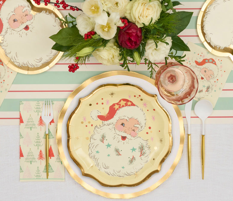 A Vintage Santa: Christmas Table for 16 festive setting featuring scalloped paper plates with a vintage Santa Claus design, gold-rimmed plates, a white and red patterned napkin, and gold-handled cutlery.