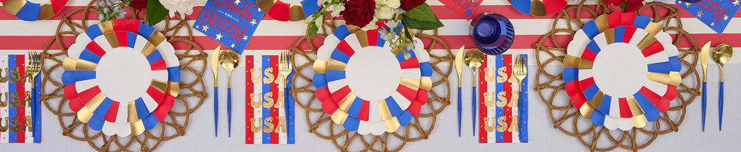 A festive table set with red, white, and blue plates, striped napkins, gold cutlery, flowers, and patriotic decorations, perfect for a 4th of July or summer celebration.