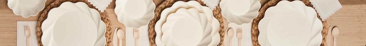Three place settings on a wooden table with white scalloped plates, woven chargers, white napkins, and wooden utensils arranged neatly.