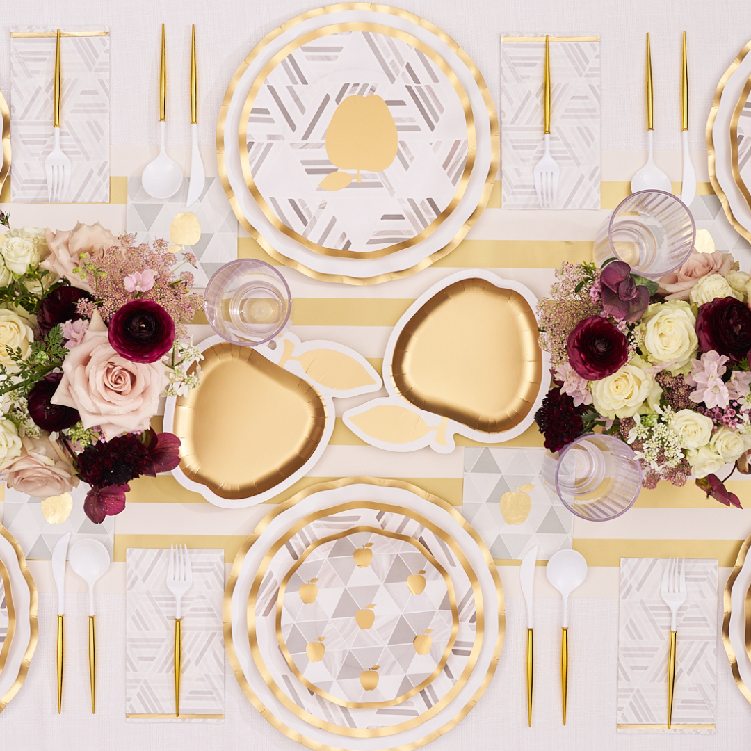 Overhead shot of a golden apple-themed table setting featuring Sophistiplate’s Golden Apple Die Cut Apple Salad Plates (8-pack), gold-rimmed tableware, pink and burgundy floral centerpieces, and white-and-gold striped linens on a light table.