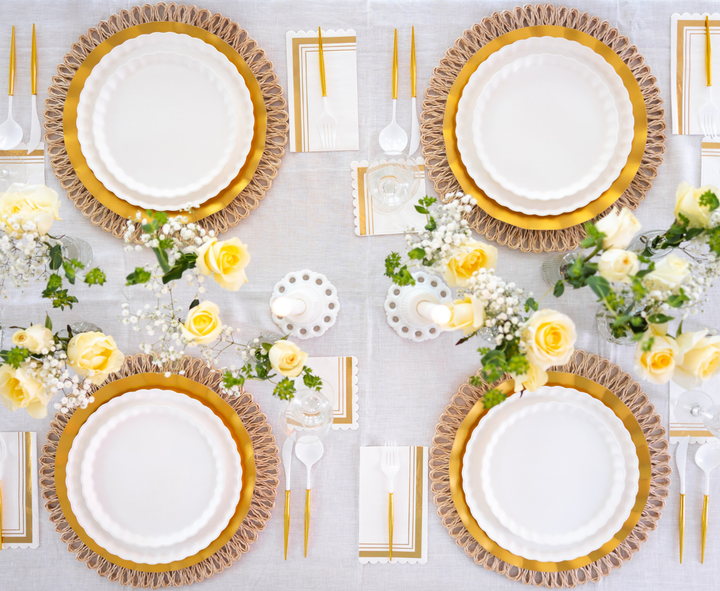 The Eco White & Gold Table Setting by Sophistiplate LLC features designer disposable plates, gold cutlery, and matching napkins on a white tablecloth, accented with yellow roses for a chic, symmetrical formal dining arrangement.