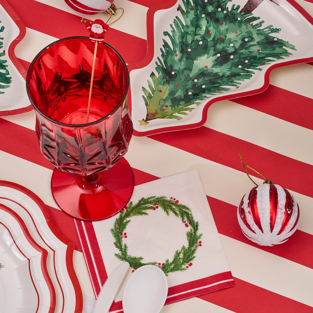 Create a festive look with the Merry and Bright Table Setting from Sophistiplate, featuring tree and stripe-shaped designer plates, a red goblet, wreath napkin, white spoon, striped ornament, and matching tablecloth.