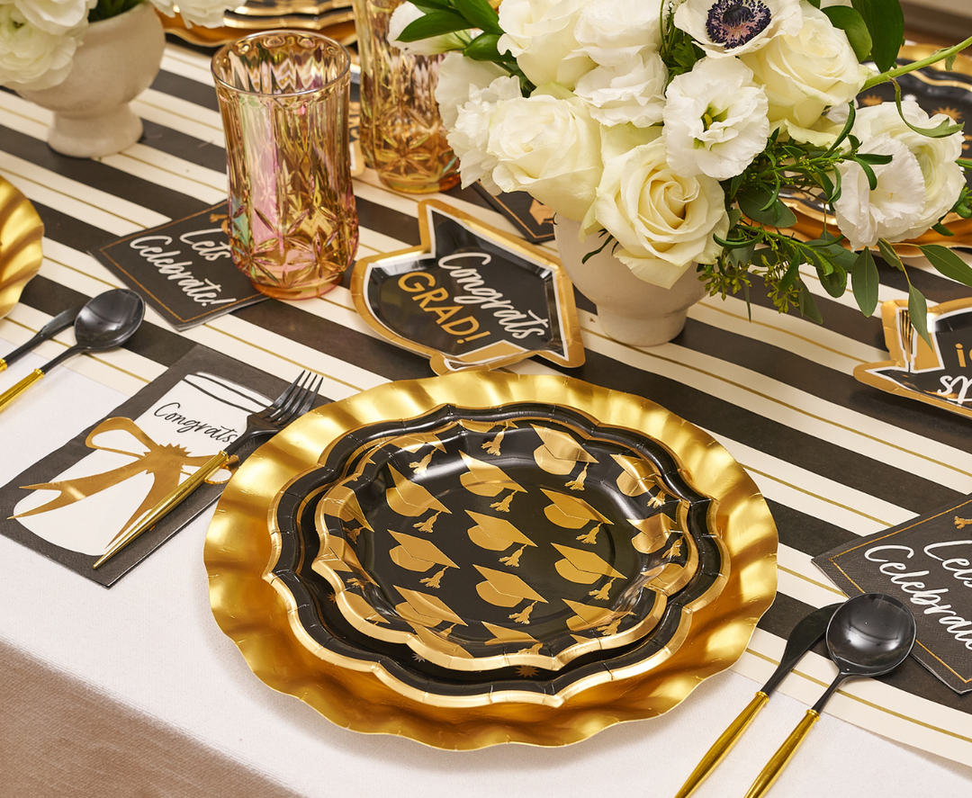 Celebrate in style with the Classic Grad Table Setting by Sophistiplate—designer plates with graduation caps, gold utensils, a striped runner, white florals, gold glasses, and "Congrats Grad" decor. The perfect disposable supplies for your graduation party!.