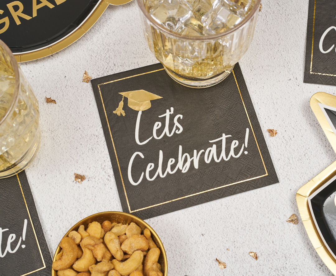 The Sophistiplate Classic Grad Cocktail Napkins (26pk) feature a black design with a gold cap and “Let’s Celebrate!”—the perfect stylish touch for your graduation party table.