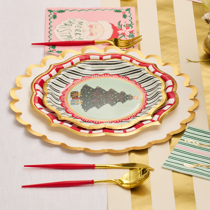 Celebrate the season with a festive table setting featuring Sophistiplate’s “Tis the Season” Salad Plates (8pk), golden and red utensils, scalloped gold-edged dinnerware, and a Merry Christmas card with Santa, all beautifully arranged on a gold and white striped tablecloth—bringing convenience and elegance to your holiday entertaining.