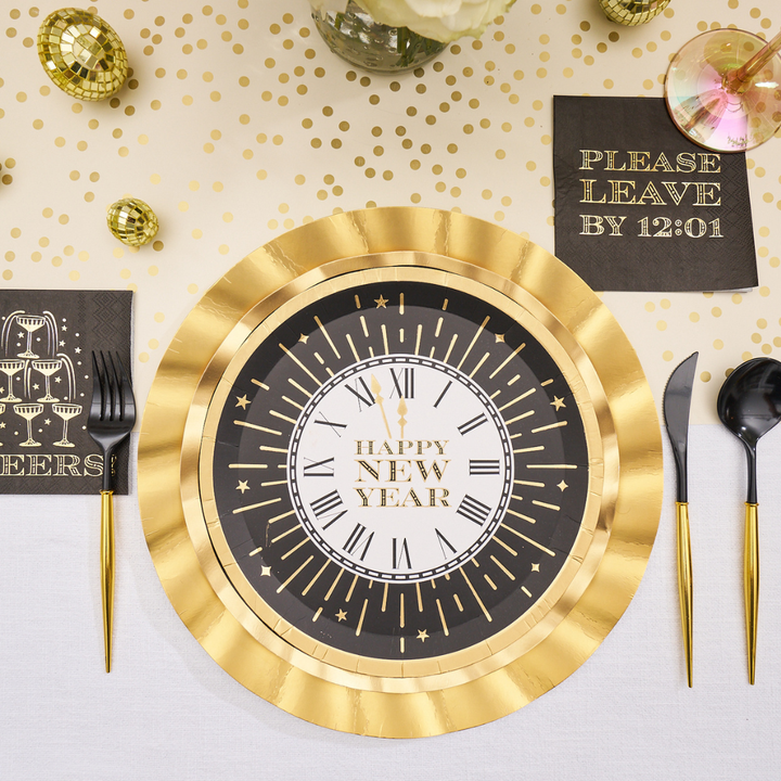 Sophistiplate Midnight Sparkle Salad Plates/8pk, designed like a black and gold clock face that reads Happy New Year, are set on a table with matching black and gold napkins and cutlery.