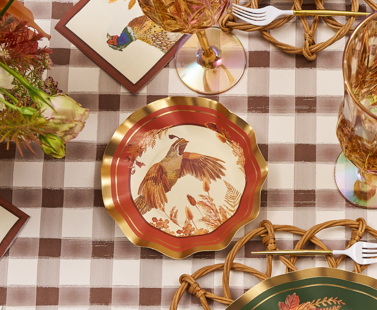A set of Sophistiplate Woodland Harvest Appetizer/Dessert Bowls (8 pack), adorned with a pheasant design and gold trim, is displayed on a brown plaid tablecloth alongside glasses, a floral napkin, woven placemats, and elegant wavy-edged appetizer bowls.