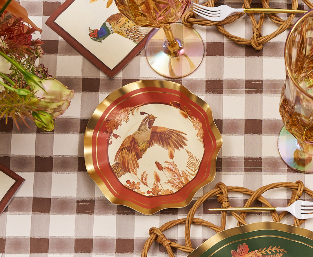 A set of Sophistiplate Woodland Harvest Appetizer/Dessert Bowls (8 pack), adorned with a pheasant design and gold trim, is displayed on a brown plaid tablecloth alongside glasses, a floral napkin, woven placemats, and elegant wavy-edged appetizer bowls.