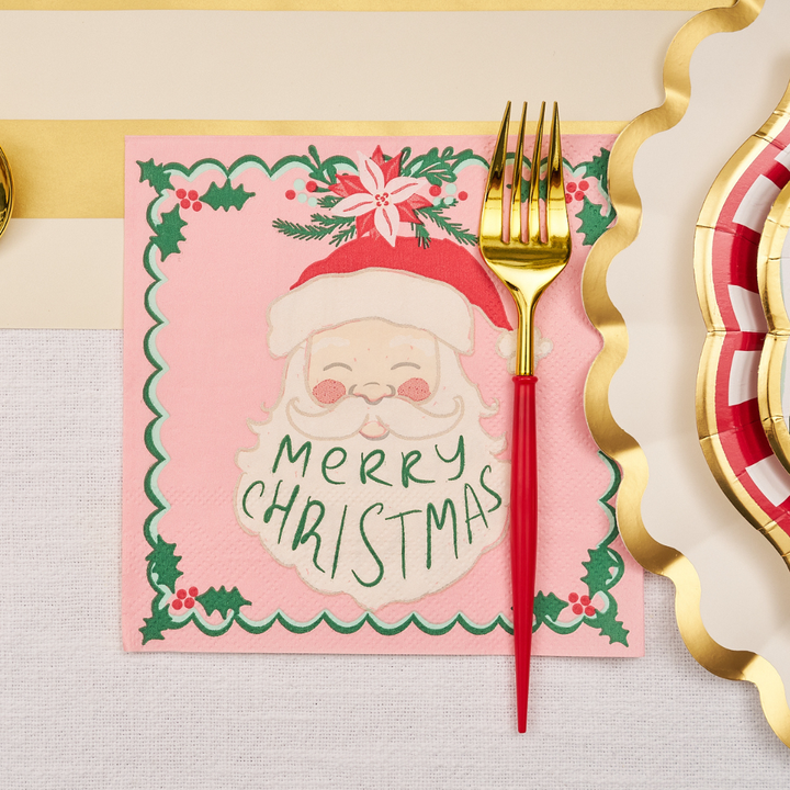 Add a touch of holiday cheer to your gatherings with the Sugarplum Tis the Season Lunch Napkins (20pk), featuring Santa’s face and “Merry Christmas” text—perfectly placed under a gold and red fork alongside a gold wavy ribbon and a festive red, gold, and white plate on your decorated table.