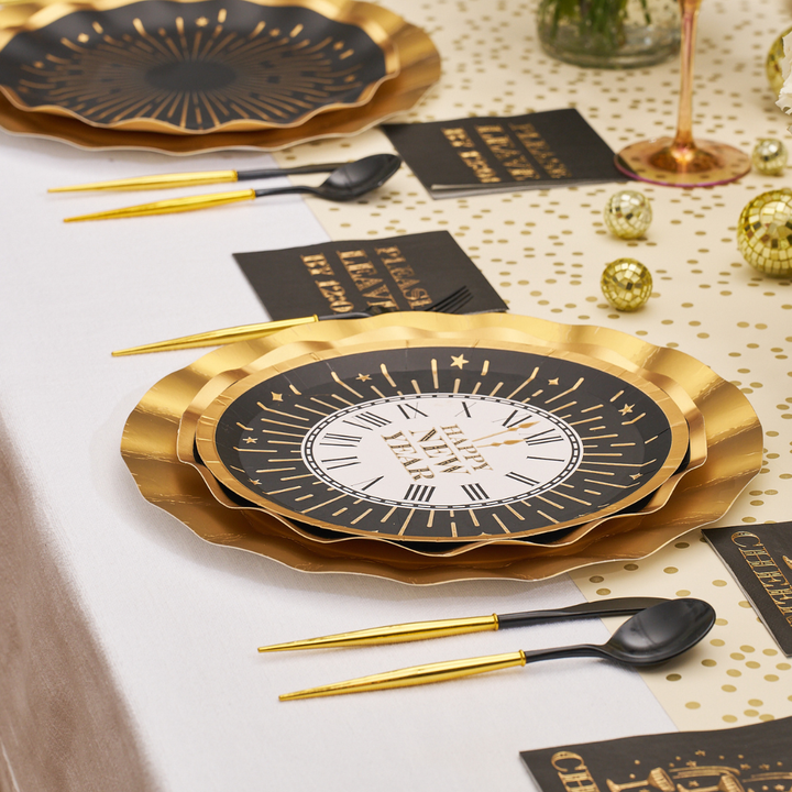 Black and gold scalloped Midnight Sparkle Salad Plates/8pk featuring a clock design, set on a table with gold-handled cutlery and matching napkins.