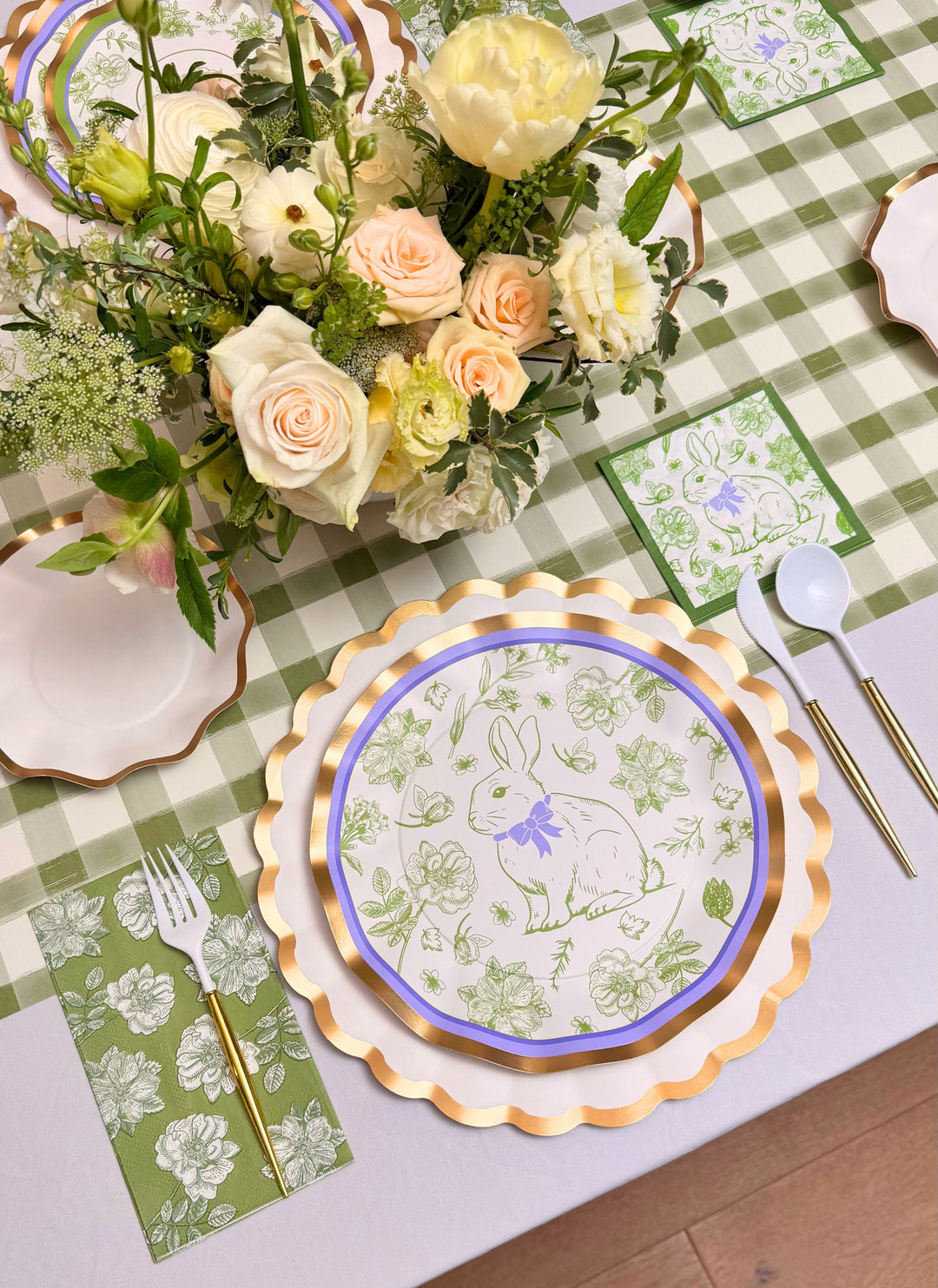 Create a spring-themed Easter table with the Sophistiplate LLC Ultimate Easter Tablescape for 16: Easter Toile, featuring floral décor, green checkered cloth, green floral napkins, gold-trimmed plates, and a bunny plate with a purple bow.