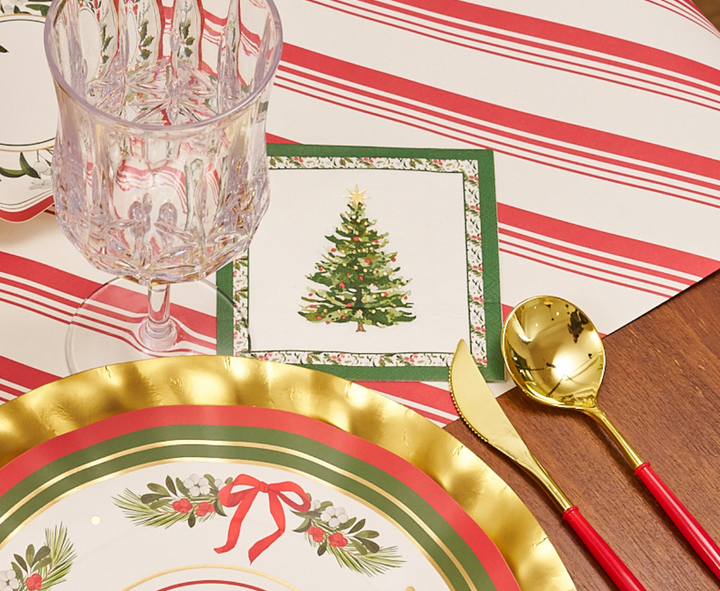 Create a celebratory holiday tablescape with Sophistiplate’s Home for the Holidays Table Setting, featuring elegant gold-rimmed designer disposable plates, coordinating gold utensils, a sparkling crystal-style glass, and a festive napkin decorated with a Christmas tree—all beautifully arranged on a cheerful red and white striped placemat.