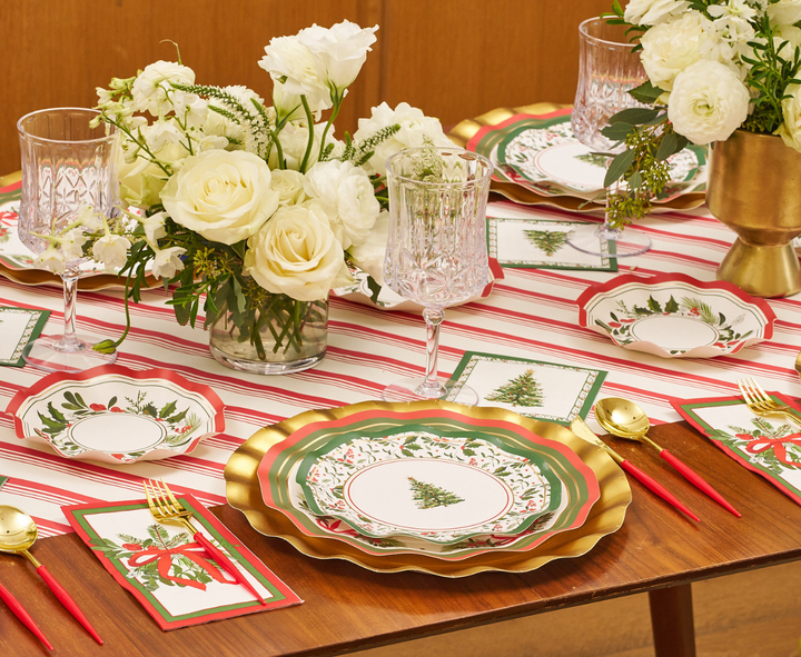 Create a festive table setting with gold-rimmed plates, holiday tree motifs, red and green accents, crystal glasses, red flatware, and white floral centerpieces atop a red-and-white striped tablecloth. Complete the look by serving your favorite treats in Sophistiplate Home for the Holidays Appetizer/Dessert Bowls (8-pack), featuring elegant wavy edges—ideal for adding sophisticated charm to your Christmas celebration.