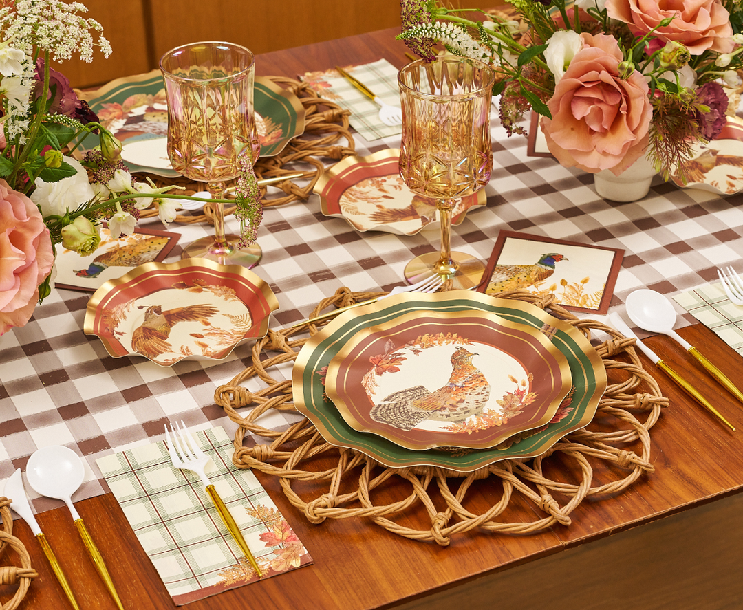 A fall-themed table setting featuring Sophistiplate Woodland Harvest Salad Plates (8pk) adorned with pheasant designs, complemented by gold-rimmed glasses, gold cutlery, plaid napkins, floral centerpieces, and a brown plaid tablecloth.