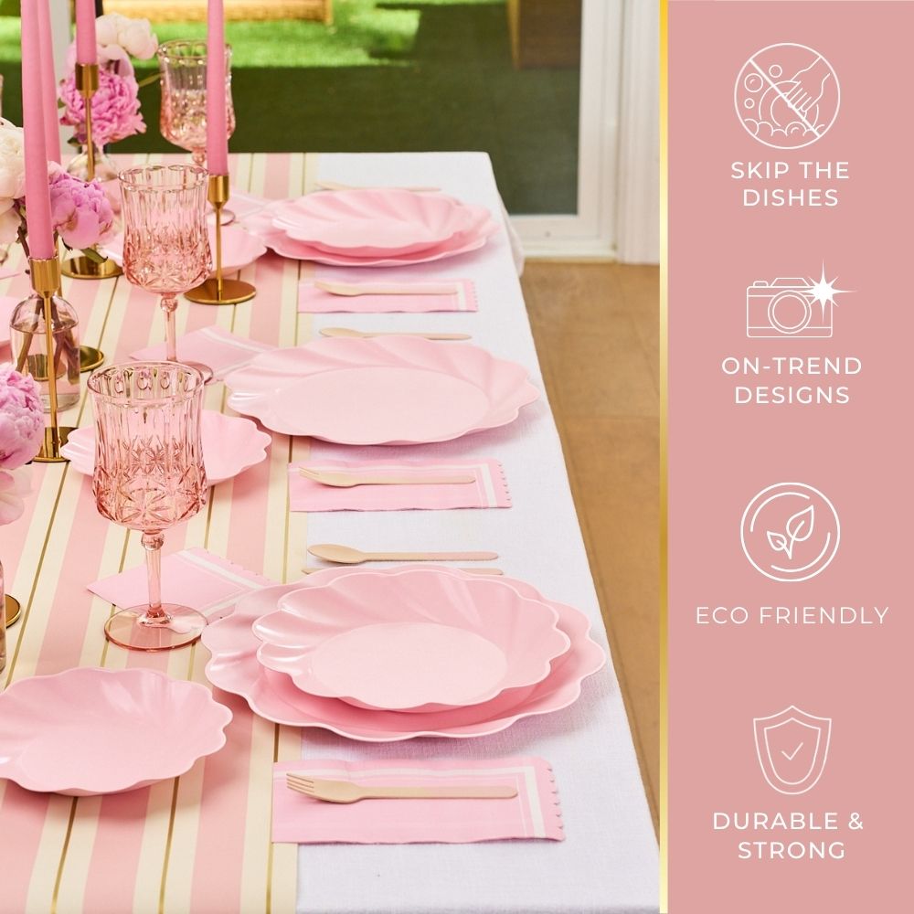 The Sophistiplate Eco-Friendly Table Setting- Blush features pink scalloped compostable party plates, pink glassware, gold flatware, and blush candles on a white cloth with pink and gold stripes—disposable, durable, and chic.