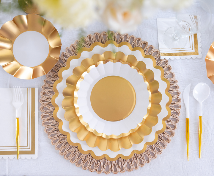 A Sophistiplate Dinner Plate Gold & White (8/pkg) creates an elegant table setting with gold utensils, a decorative placemat, a napkin, and clear glasses on a white tablecloth.