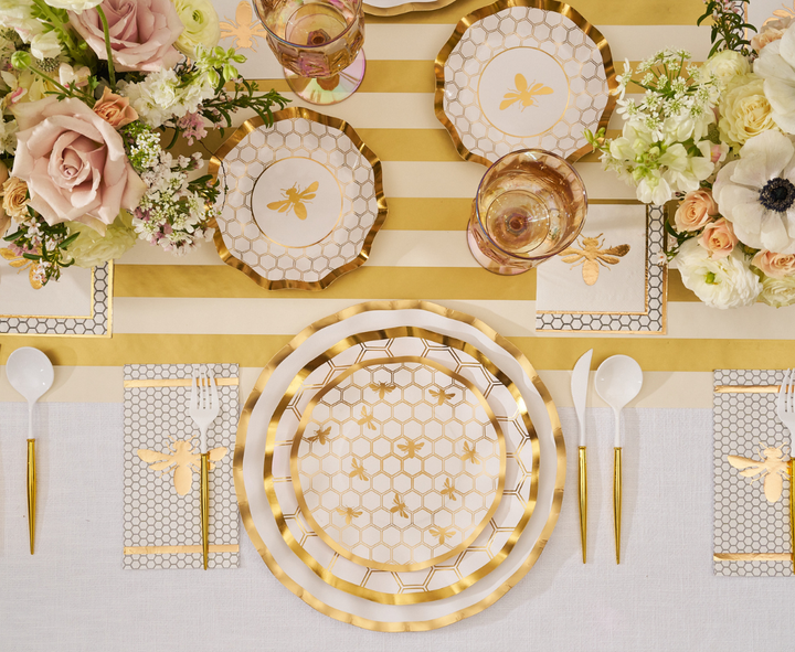 Create an elegant tablescape with the White Honeybee Table Setting by Sophistiplate, featuring gold and white plates adorned with charming bee and honeycomb designs. Complete the look with gold utensils, floral centerpieces, and a striped table runner. Glassware and napkins coordinate beautifully with the bee-themed decor, while elegant disposable dinnerware such as gold-rimmed paper plates from Sophistiplate adds a sophisticated yet convenient touch for effortless entertaining.