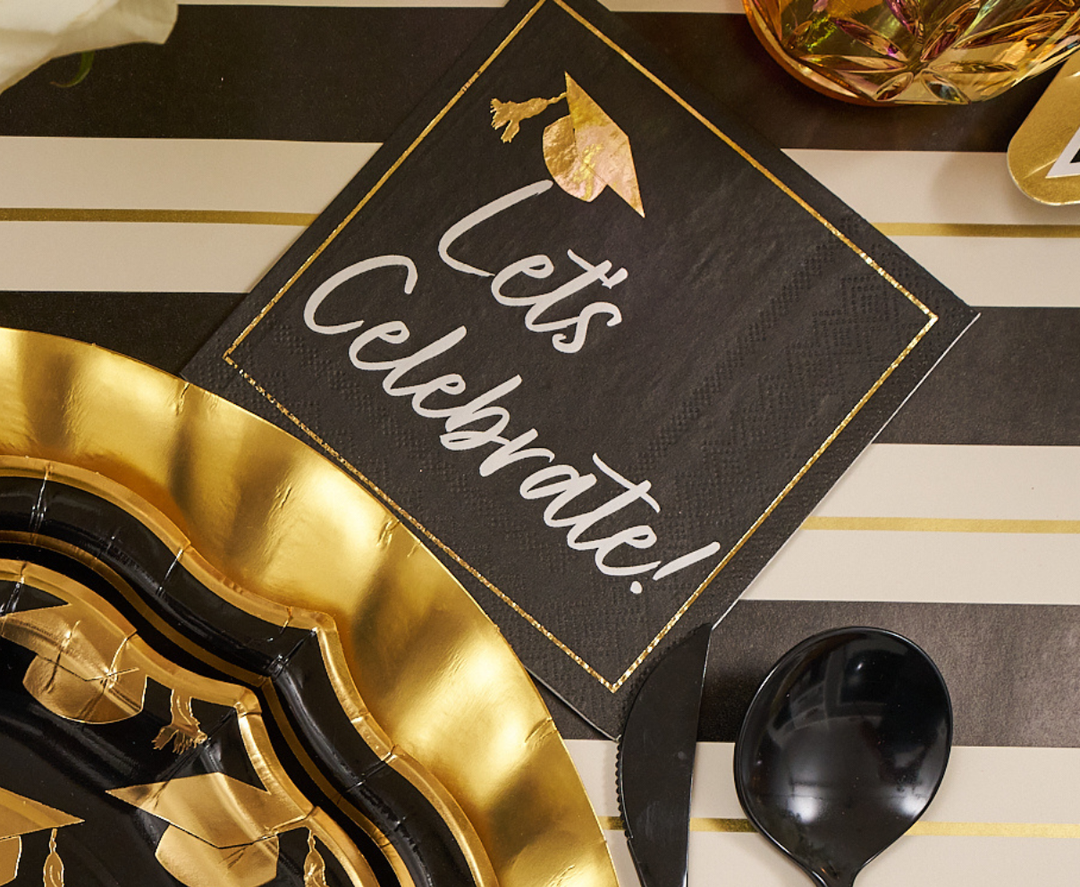 The Sophistiplate Classic Grad Table Setting features a black napkin with a gold graduation cap and "Lets Celebrate!" in white script, paired with stylish designer plates—a perfect addition to your graduation party supplies.