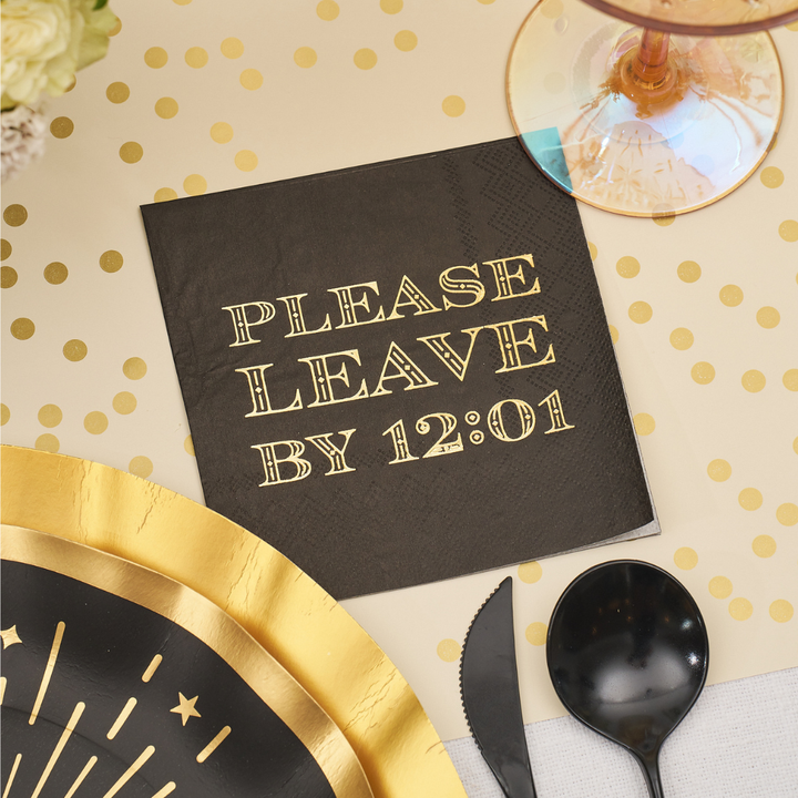 A black Midnight Sparkle Paper Cocktail Napkin Please Leave By 12:01 /26pk with gold-printed text, arranged among gold-rimmed plates and cutlery.
