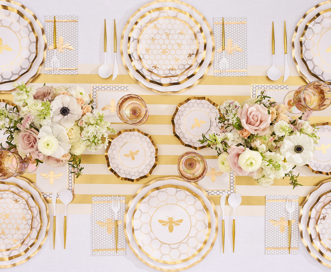 Create a sophisticated tablescape with the Sophistiplate White Honeybee Table Setting featuring honeycomb and bee-themed elegant paper plates with shimmering gold accents, gold utensils, and coordinating napkins. Paired with floral centerpieces and a striped runner, this symmetrical arrangement is festive and perfect for gatherings that demand both style and convenience. Enjoy effortless entertaining with these beautiful disposable plates from Sophistiplate.