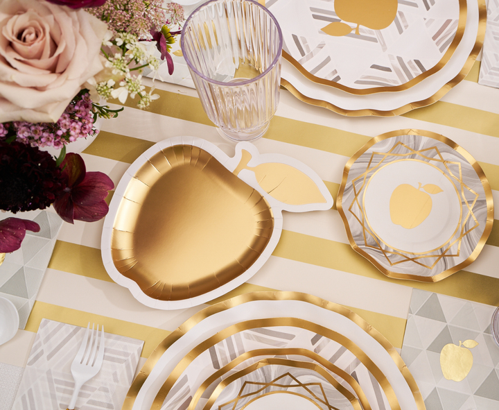 The Sophistiplate Golden Apple Table Setting features a gold apple-shaped plate, a beautiful floral arrangement, a striped tablecloth, and coordinated disposable plates, cups, and cutlery—offering an elegant and festive option for celebrating Rosh Hashanah.