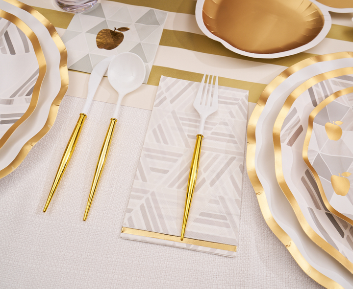 Sophistiplate’s Golden Apple Table Setting features white and gold plates, disposable cutlery in coordinating shades, and patterned napkins adorned with geometric apple designs, all elegantly arranged on a cream tablecloth with gold-accented decor—perfect for creating a sophisticated Rosh Hashanah celebration.