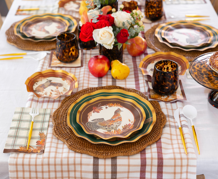 Create a cozy autumn atmosphere with the Sophistiplate Woodland Harvest Table Setting, featuring designer rooster paper plates, woven chargers, tortoiseshell cups, gold utensils, plaid napkins, and a crisp white tablecloth. Complete the look with a centerpiece of red and white flowers accented by apples and pears for the perfect fall gathering.
