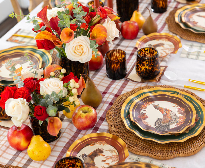 The Woodland Harvest Table Setting by Sophistiplate features autumn-themed designer paper plates, woven placemats, floral centerpieces, apples, pears, and tortoiseshell glasses on a plaid tablecloth—creating the perfect harvest party decor.