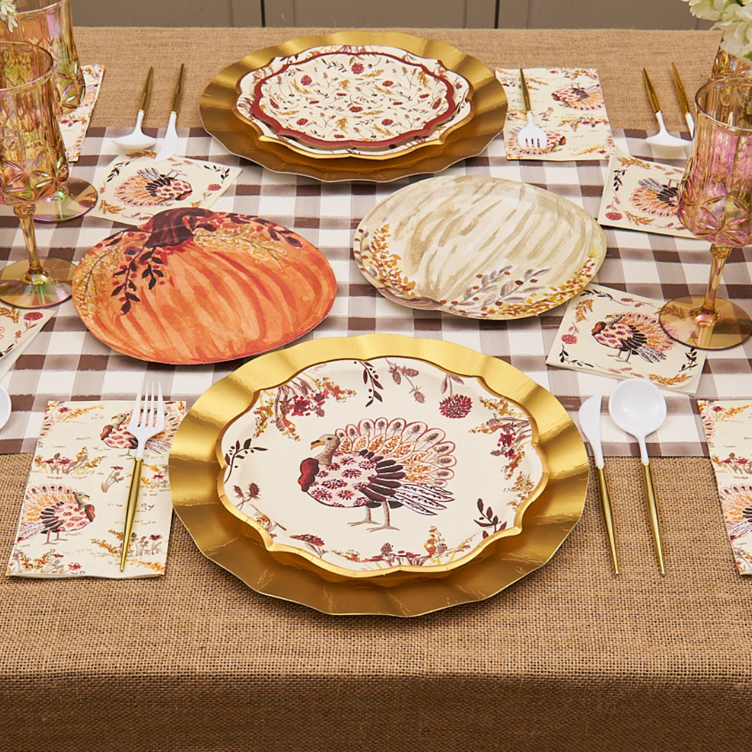 A Thanksgiving table setting featuring Sophistiplate Amber Harvest Dinner Plates (8pk), gold utensils, floral napkins, wine glasses, and a plaid table runner on a burlap tablecloth.