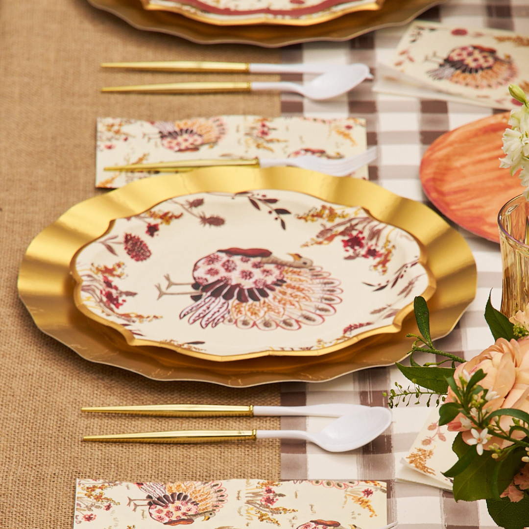 A table set with Sophistiplate’s Amber Harvest Dinner Plates (8-pack), featuring gold utensils, floral napkins on a checkered tablecloth, orange flowers in a vase, and a peach-colored plate beside the setting.