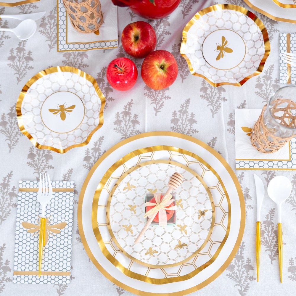 Create an elegant and festive Rosh Hashanah table setting with the Sophistiplate LLC Rosh Tablescape for 16 Guests: White Honeybee. This bee-themed set features gold and white designer disposable plates, gold utensils, apples, a honey dipper gift, and a patterned tablecloth for a beautiful holiday celebration.