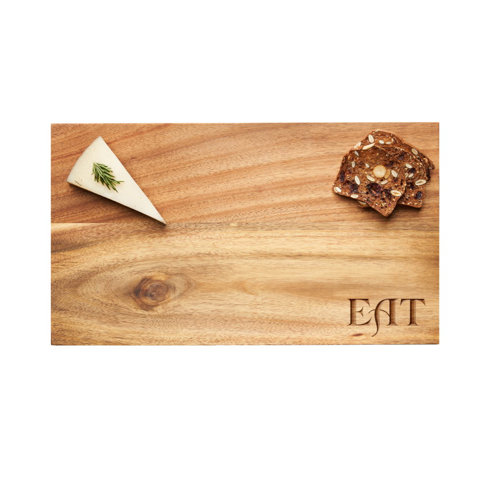 A Maple Modern Acacia Rectangle serving board, featuring the word “EAT” engraved in a Parisian font, measures 14 x 8″ and is elegantly arranged with a slice of cheese garnished with rosemary on the left and a stack of crackers on the right.