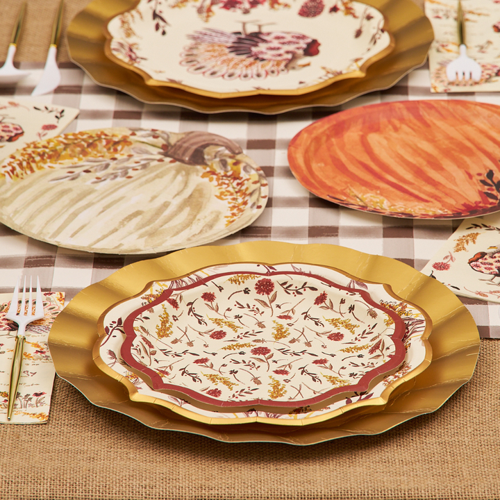 A fall-themed table setting featuring Sophistiplate Amber Harvest Salad Plates (8pk) with decorative pumpkins and leaves, paired with gold chargers, a plaid table runner, burlap tablecloth, gold utensils, and autumn-patterned napkins.