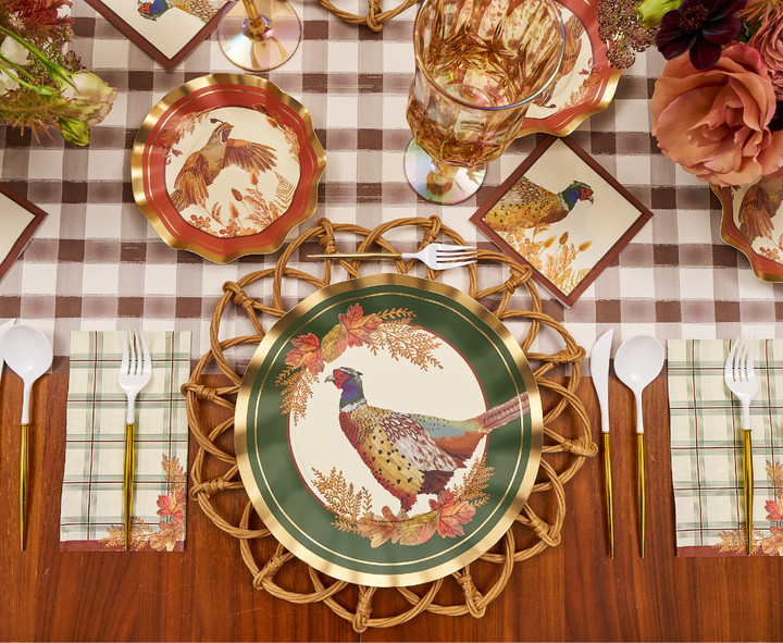 A fall-themed table setting with Sophistiplate Woodland Harvest Dinner Plates (8pk) adorned with pheasant illustrations, paired with coordinating napkins and cups, gold cutlery, and an autumn floral centerpiece atop a brown plaid tablecloth.