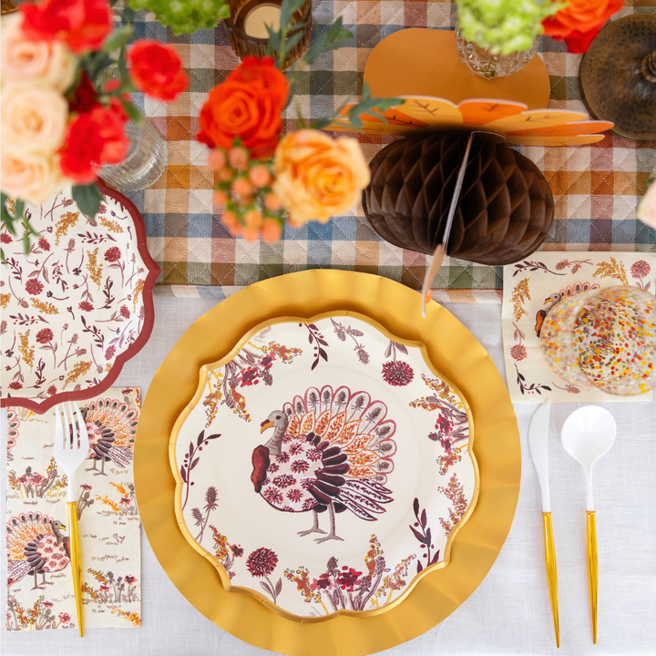 Create a festive Thanksgiving tablescape with the Amber Harvest Table Setting by Sophistiplate, featuring turkey-themed designer disposable plates, gold chargers, floral napkins, gold utensils, and autumn blooms atop a plaid tablecloth. The elegant Amber Harvest collection adds sophistication to your celebration, with a charming honeycomb turkey decoration completing the look.