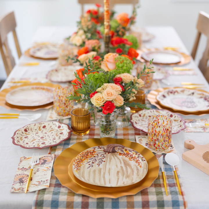 Celebrate the season with the Amber Harvest Table Setting by Sophistiplate—a festive dining arrangement featuring autumn-themed plates adorned with pumpkin and leaf designs, elegant gold flatware, floral centerpieces, and a stylish checkered tablecloth. Vibrant cups and neatly arranged napkins complete this designer disposable set, making it perfect for highlighting your autumn party supplies.