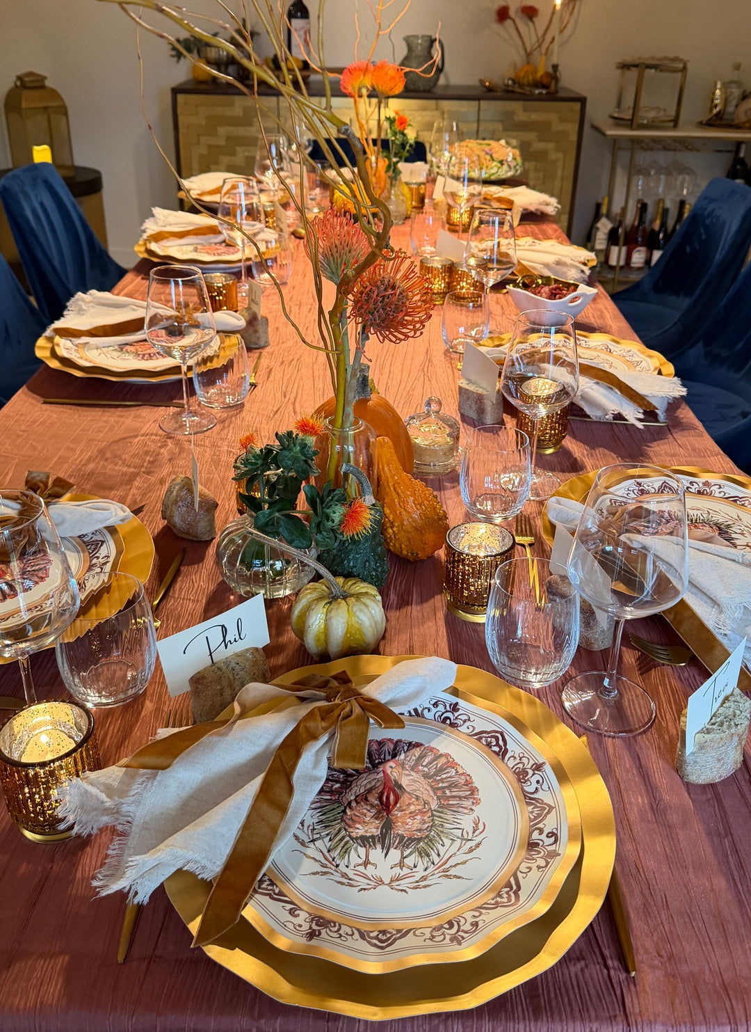A Sophistiplate LLC Turkey & Gourds: Thanksgiving Table for 16 set on a mauve tablecloth with velvet ribbons, gourds, and floral centerpieces.