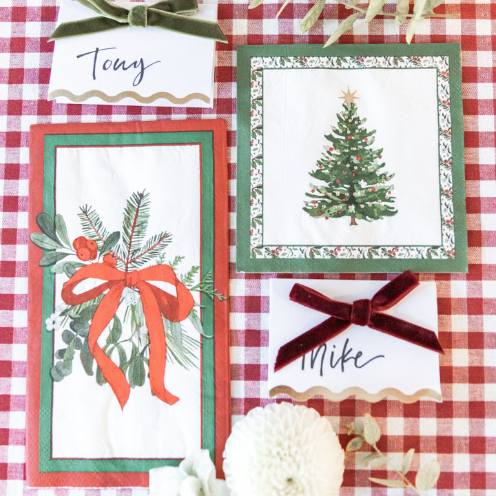 A Home for the Holidays: Christmas Table for 16 setting on a red and white checkered tablecloth, with heavy duty paper plates, mistletoe-patterned napkins, and two place cards with velvet ribbons hand-lettered for Tony and Mike.