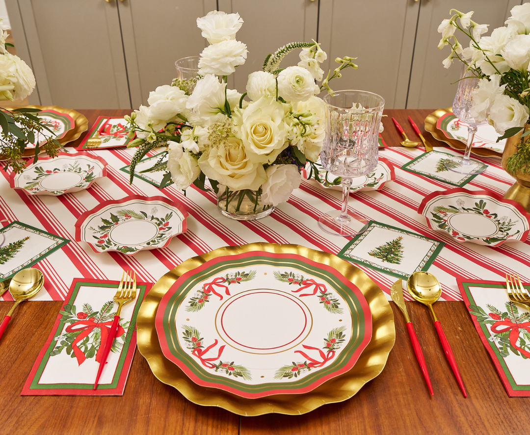 Create a festive holiday table setting with Sophistiplate Home for the Holidays Dinner Plates (8pk), featuring Christmas tree and wreath designs. Pair them with gold, red, and green plates, a striped tablecloth, gold utensils, crystal glasses, white floral centerpieces, and matching napkins for an elegant seasonal touch.