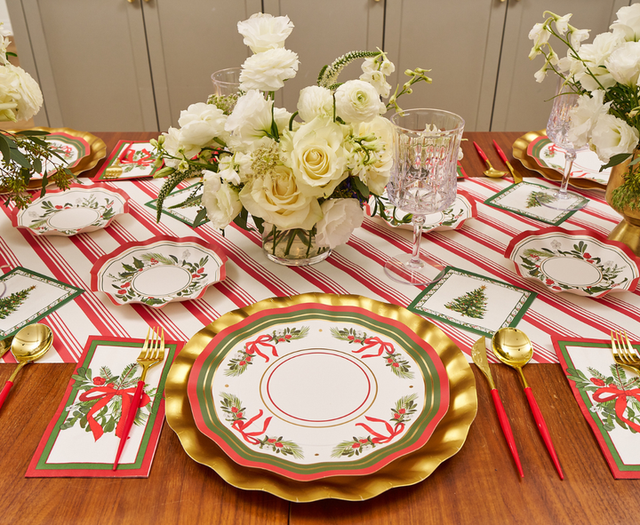 Create a festive holiday table setting with Sophistiplate Home for the Holidays Dinner Plates (8pk), featuring Christmas tree and wreath designs. Pair them with gold, red, and green plates, a striped tablecloth, gold utensils, crystal glasses, white floral centerpieces, and matching napkins for an elegant seasonal touch.