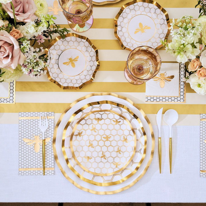 The White Honeybee Table Setting by Sophistiplate sets the scene in this arrangement, featuring gold and white hexagon-patterned plates with gold rims, coordinating gold utensils, charming bee motifs, floral arrangements, and a striped table runner. Even the napkins and cups highlight bee designs for a cohesive, festive look—all while making entertaining effortless with these stylish disposable plates.