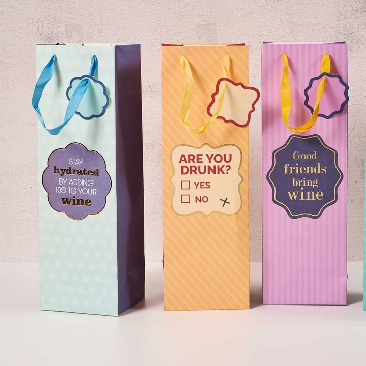 The Drinks On Me Stay Hydrated-Wine Bag set includes three upright, reusable bags with funny sayings, handles, and gift tags—perfect hostess gifts for wine lovers.