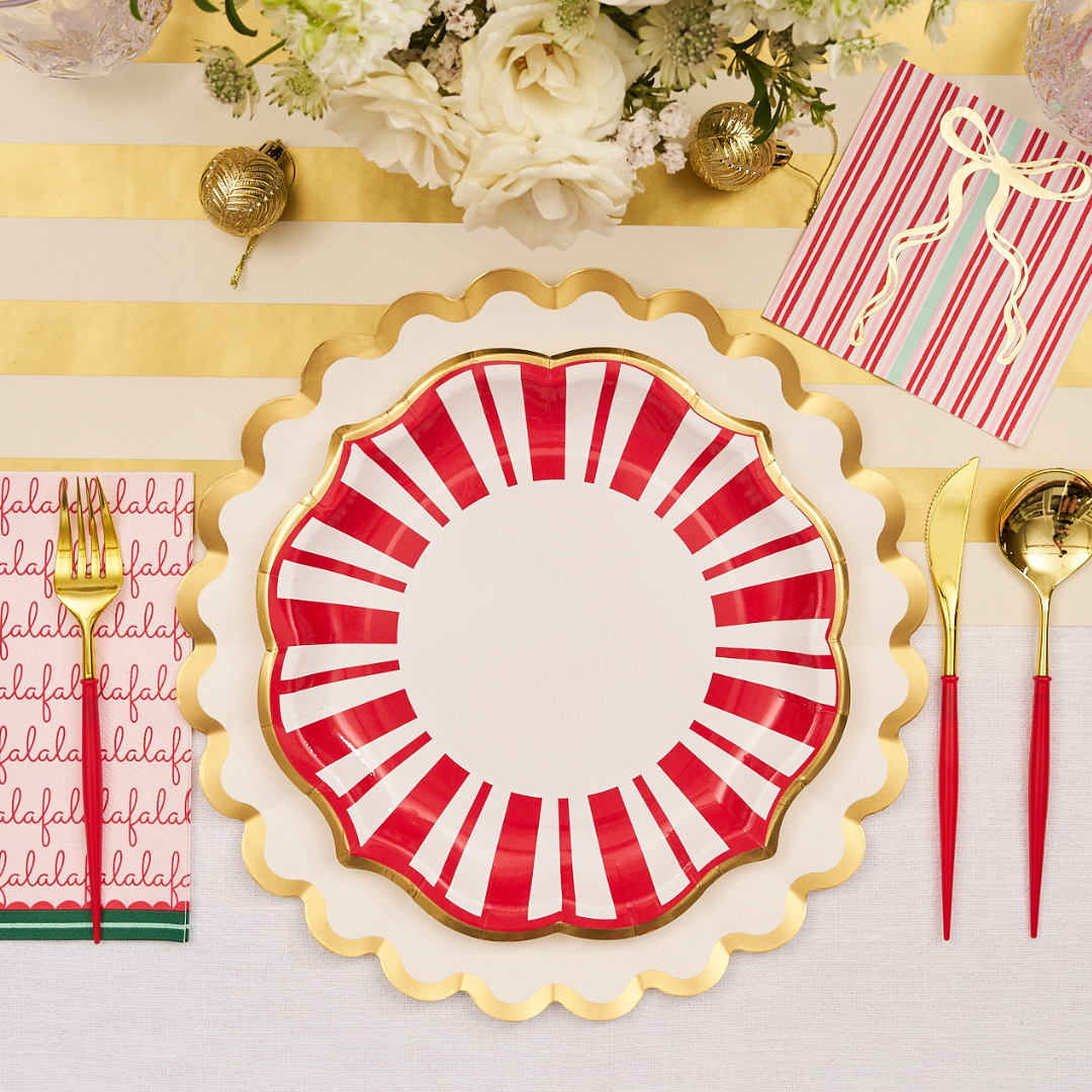 Create a festive tablescape with Sophistiplate’s Tis the Season Dinner Plates (8pk): bold red and white plates layered over gold-rimmed chargers, complemented by gold cutlery with red handles, cheerful striped and “fa la la” napkins, and fresh white blooms atop a striped gold-and-white tablecloth. Perfect for holiday gatherings, these convenient paper plates capture the spirit of the season while adding elegance to your celebration.