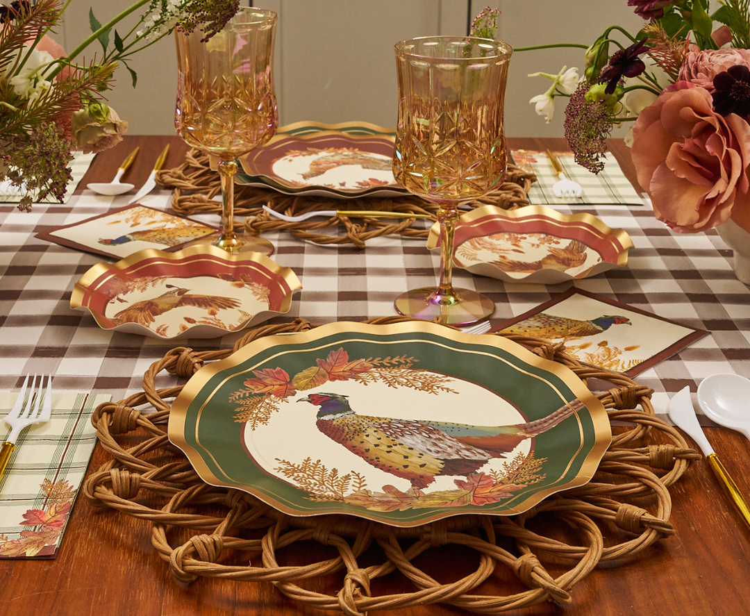 A fall-themed table setting featuring Sophistiplate Woodland Harvest Dinner Plates (8pk), woven placemats, plaid napkins, gold-rimmed glasses, and autumn flowers atop a brown and white checkered tablecloth.